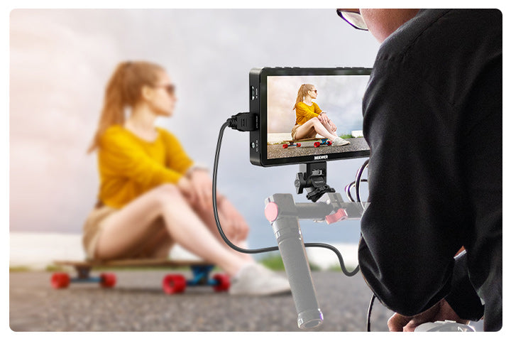 A content creator films a video of a girl sitting on a skateboard, and using an OLED camera monitor to view the footage