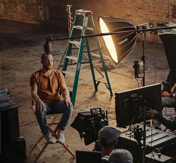 Man seated in a film set with lighting and camera equipment.