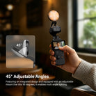 A hand holding a DJI Osmo Pocket 4 equipped with an attached NEEWER Pocket 4 LED fill light, capturing a selfie in a dim indoor setting.