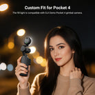 A woman takes a selfie at night using a DJI Osmo Pocket 4 with an attached NEEWER M29 Mini LED Fill Light.